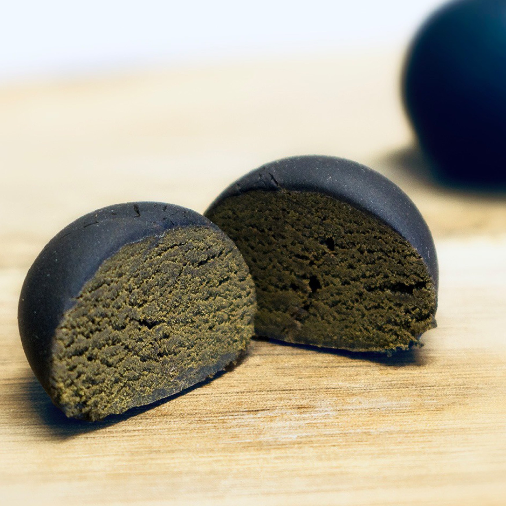 Eine Nahaufnahme von CBD Hasch, das auf einem Holzbrett liegt. Ein Stück des premium schweizer CBD Haschs ist in der Mitte geteilt, sodass die wunderschöne innere Struktur voller potenter Trichomen sichtbar ist.